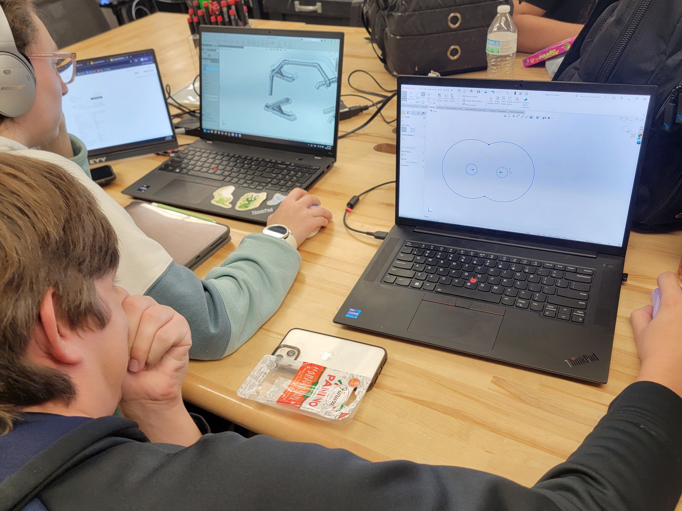 Team members measuring a robot frame in the lab, with computer vision code on a monitor in the foreground