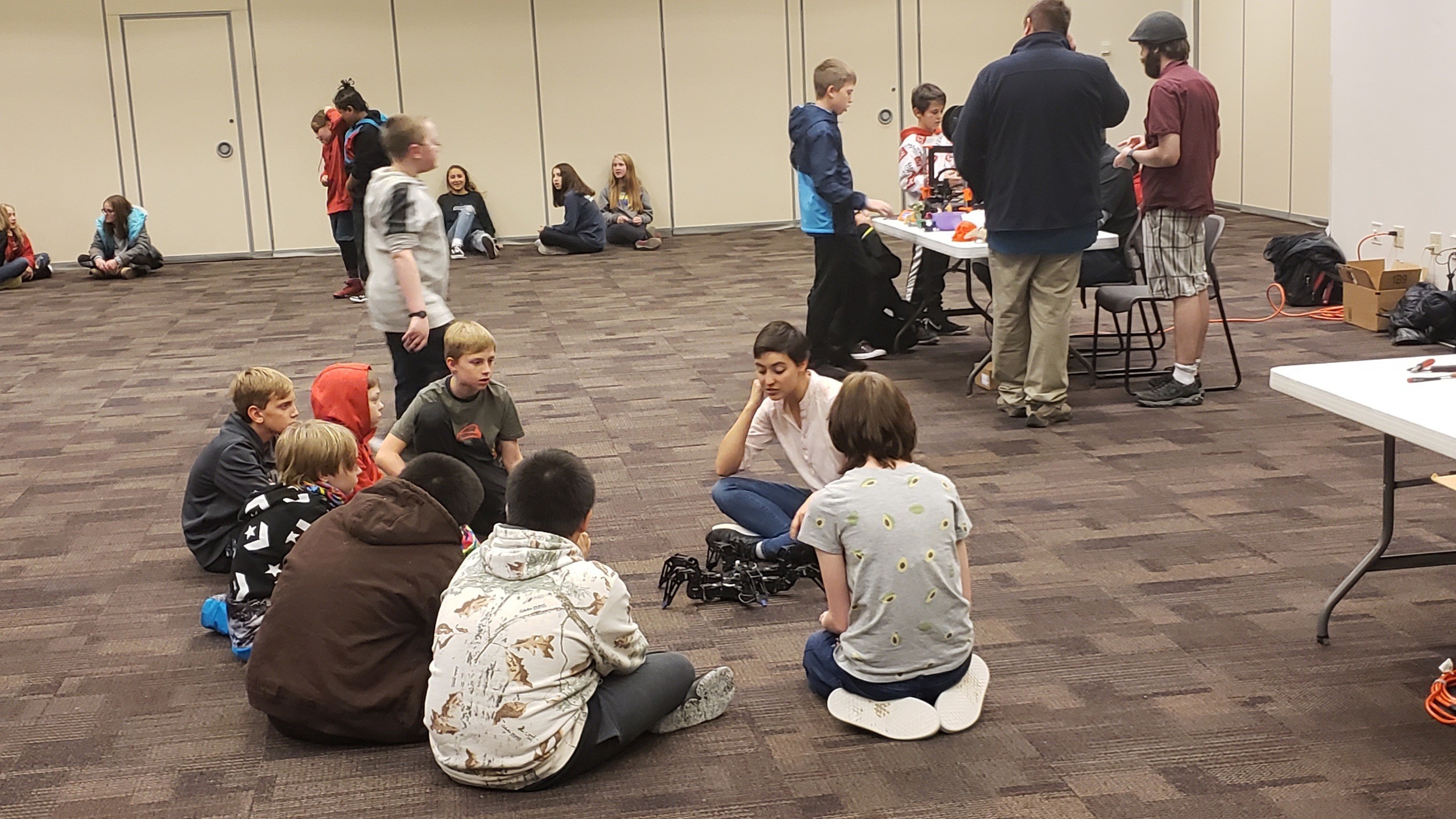 Team members demonstrating a robot to a group of school students sitting on the floor
